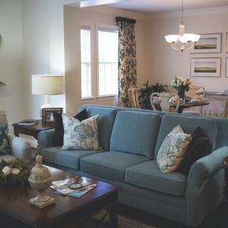 A cozy living room with a blue sofa and a dining area in the background.