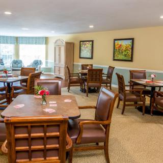 A cozy dining area with wooden tables and chairs, adorned with paintings and soft lighting.
