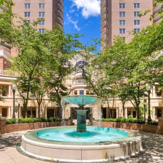 A beautiful courtyard with a central fountain surrounded by trees and high-rise buildings under a clear blue sky.