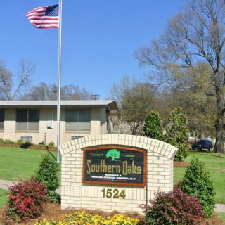 A brick sign for Southern Oaks Residential Center with an American flag flying nearby, surrounded by landscaped greenery and trees.