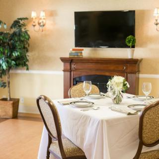 A neatly set dining table in a cozy room with a fireplace and television.