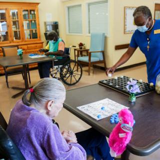 A caregiver assists elderly residents in a nursing home, promoting social interaction and engagement through activities like board games.