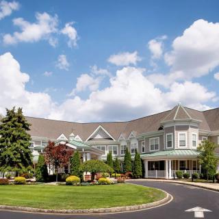 A picturesque view of a large building surrounded by lush greenery under a blue sky with scattered clouds.