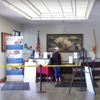 A woman standing at a counter in an office lobby, surrounded by informational signage and flags.