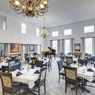 A spacious and elegant dining room featuring white tablecloths, a grand piano, and ornate chandeliers.