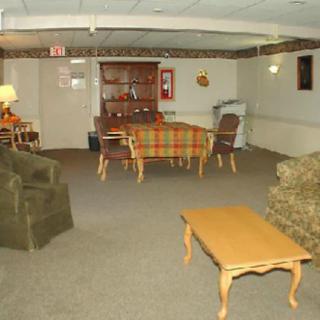 A cozy basement room with a dining table, chairs, sofa, and lamp.