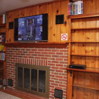 A cozy living room with a brick fireplace, wood-paneled walls, a mounted TV, and built-in shelves.