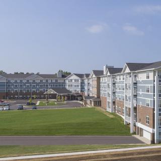 A suburban residential apartment complex with expansive grassy areas under a clear blue sky.