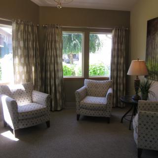A cozy living room with armchairs, a small table, and a lamp by the window allowing natural light.