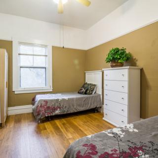 A cozy bedroom featuring twin beds with floral bedding, a dresser with a potted plant, and hardwood flooring.