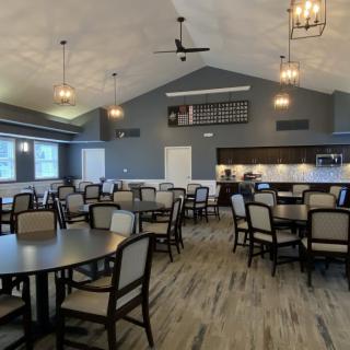 A spacious dining area with tables and chairs, featuring a kitchen area and stylish lighting.
