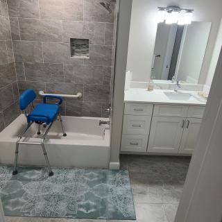 A modern bathroom with a bathtub, accessible chair, and vanity sink.