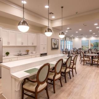A modern kitchen and dining area with white cabinets, a long countertop, elegant chairs, and stylish pendant lighting.