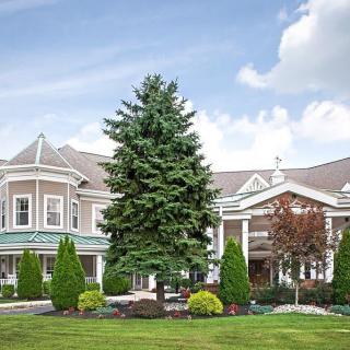 A large, elegant building with manicured landscaping and a prominent tree in front under a partly cloudy sky.