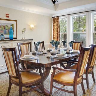 A well-furnished dining room with a large table and elegant chairs, featuring natural light from the windows and tasteful decorations.