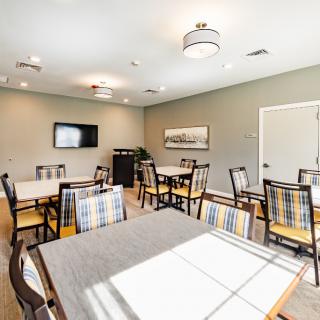 A modern meeting room with several tables and chairs, featuring a television on the wall and bright lighting.