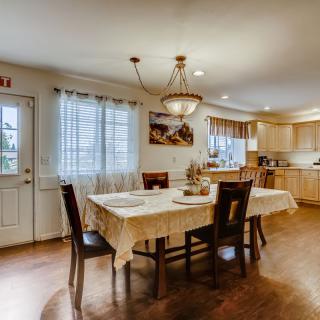 A cozy dining area with a table set for four, adjacent to a kitchen with warm lighting and wood flooring.