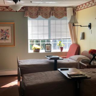 A cozy patient room featuring two beds, natural light pouring in from the window, and decorative touches for a comforting atmosphere.