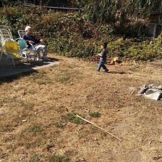 A child playing in a garden while an elderly person relaxes on a sun chair.