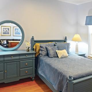 A cozy bedroom with a blue-themed decor, featuring a bed, dresser with mirror, and a lamp.