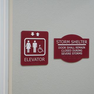A pair of signs indicating the locations of an elevator and a storm shelter, emphasizing accessibility features and safety instructions.
