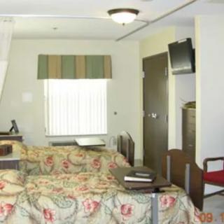 A cozy bedroom with floral bedding, a wall-mounted television, and a window with striped curtains.