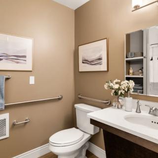 A modern bathroom with neutral tones, featuring a toilet, sink with mirror, and decorative elements like flowers and paintings.