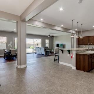 A modern open-concept living space featuring a kitchen, dining area, and living room with tile flooring and pendant lighting.