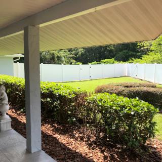 A view of a well-maintained yard with a white fence and neatly trimmed bushes from the patio.