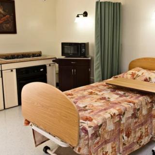 A hospital room featuring a bed with a floral-patterned cover, medical equipment, and simple furnishings.