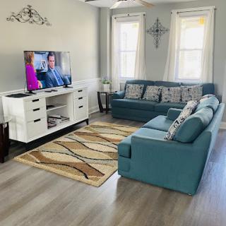 A cozy and modern living room featuring a teal sofa, a stylish rug, and a television.