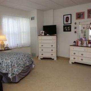 A cozy bedroom featuring a bed, dresser, mirror, and lamp with soft lighting.