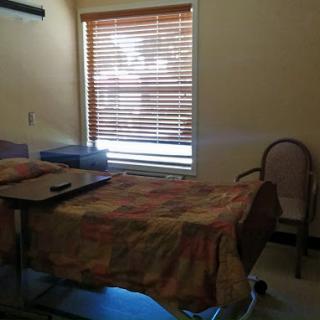 A quiet hospital patient room with a bed, adjacent furniture, and natural light coming through the window.