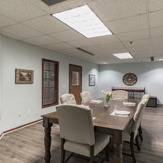 A modern conference room with a large wooden meeting table and cushioned chairs, decorated with wall art and subtle lighting.
