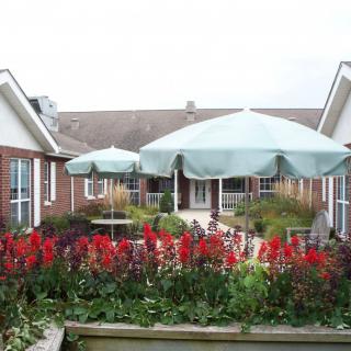 A beautiful garden patio with colorful flowers and large umbrellas in front of a brick building.