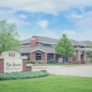 A view of a brick office building with a sign in front and surrounding greenery.