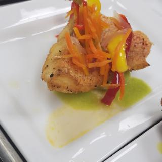 A beautifully plated seafood dish topped with colorful sauted vegetables.