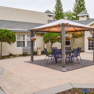 A cozy outdoor patio area featuring a gazebo with chairs and a table, surrounded by landscaped greenery.
