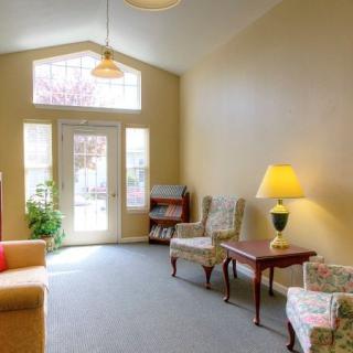 A cozy living room with a sofa, armchairs, and a coffee table, illuminated by natural light through large windows.