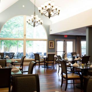 A spacious dining room with elegant chandeliers, wooden flooring, and large windows letting in natural light.