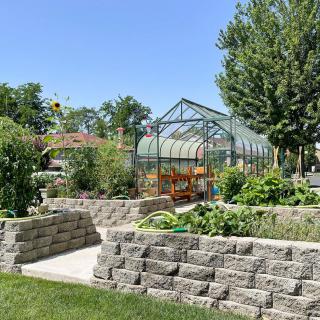 A beautiful garden with a greenhouse surrounded by lush greenery and blue skies.