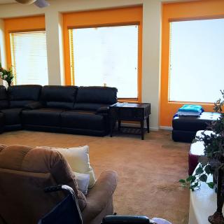 A cozy living room with a large sofa, armchair, and several windows letting in natural light.