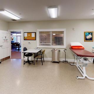 A clean and organized examination room in a clinic, featuring a medical table and desk.