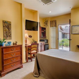 A cozy and well-furnished bedroom featuring a bedside dresser, desk area, and a view through the window.