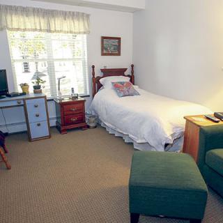 A cozy bedroom featuring a single bed, a desk with a chair, and natural light coming through the window.