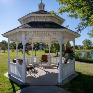A quaint white gazebo with outdoor furniture, set in a scenic park by the lake.