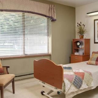 A well-lit hospital room with a single bed, chair, and window.