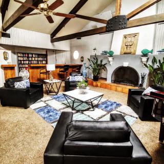 A stylish living room features modern furniture, exposed ceiling beams, and a cozy fireplace surrounded by plants.