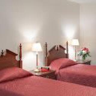A cozy hotel room featuring twin beds with a nightstand and lamps.