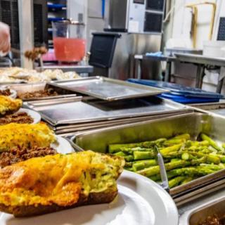 A buffet setup featuring stuffed potatoes with melted cheese and a tray of asparagus in a kitchen setting.